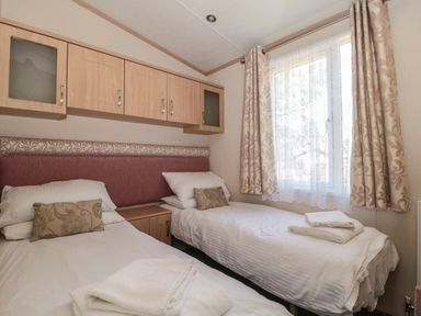 A bedroom with two single beds bedside table above bed cabinets and a window with curtains at Birch in Swanage