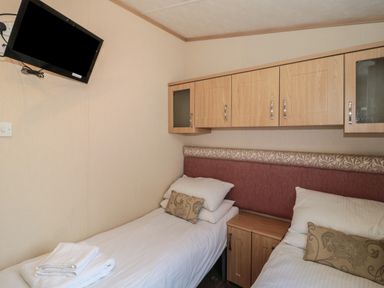 A bedroom with two single beds a wall mounted TV and wooden overhead cabinets at Birch Swanage