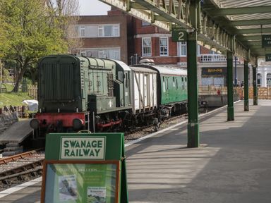 A vintage train on tracks at platform 2 at Swanage Railway station with a green signboard in front