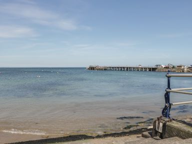 A view of the sea with a sandy beach a pier in the distance and a metal railing at Birch in Swanage