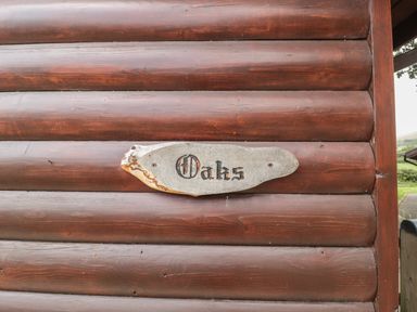 A wooden log cabin wall with a wooden sign reading Oaks at Oaks Swanage
