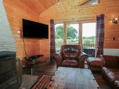 A wooden living room with leather armchairs a wooden table a wall-mounted television and glass doors at Oaks in Swanage