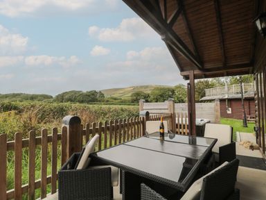 A covered outdoor patio with a glass table and four chairs overlooking fields and hills at Oaks Swanage