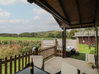 A covered wooden patio with table and chairs overlooking a fenced grassy area and fields at Oaks Swanage
