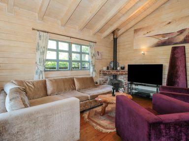 A living room with a large sofa a wooden coffee table two purple armchairs a fireplace and a television at Cherry in Swanage