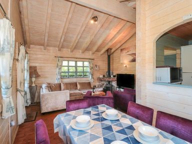 A dining table set with four white bowls and plates and purple chairs in a wooden living room with a beige sofa a television and wood stove at Cherry in Swanage