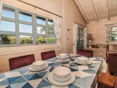 A dining table with dishes and bowls and red chairs in a wooden room with blue windows and a seating area at Cherry in Swanage