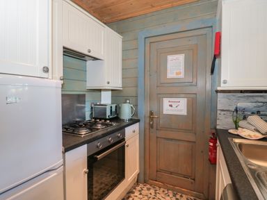 A kitchen with white cabinets a gas stove oven refrigerator toaster kettle sink and a wooden door with signs at Cherry in Swanage