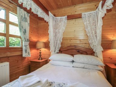 A bedroom with a wooden bed with white linens and lace curtains and bedside tables with lamps at Cherry in Swanage