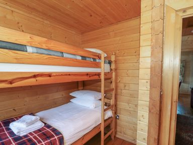 A wooden bunk bed with white bedding and folded towels in a wooden room at Cherry in Swanage