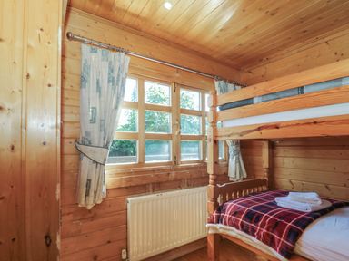 A wooden bedroom with bunk beds and a window with curtains at Cherry in Swanage