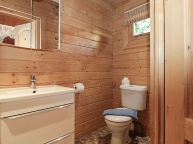 A bathroom with a sink cabinet, a mirror, a toilet with towel and toilet paper in a wooden cabin at Cherry Swanage