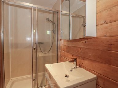 A bathroom with a glass-enclosed shower and a white sink with a faucet against a wooden wall at Cherry in Swanage