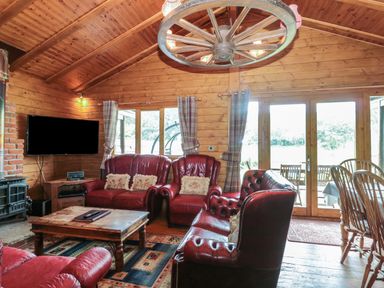 A wooden living room with red leather sofas a wooden coffee table a television and large glass doors at Walnut in Swanage