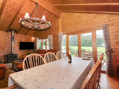 A wooden dining room with a table and chairs next to large windows overlooking a garden at Walnut in Swanage