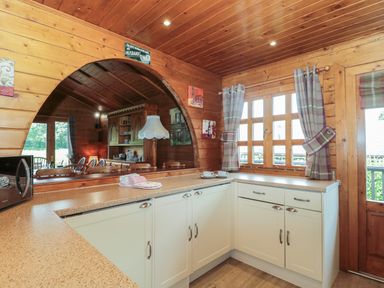 A kitchen with beige cabinets a microwave and a window with plaid curtains at Walnut in Swanage