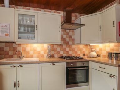 A kitchen with cream cabinets, a gas stove, oven, sink, kettle, and tiled backsplash at Walnut in Swanage