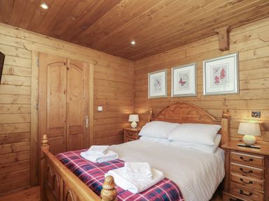 A bedroom with wooden walls ceiling bed bedside tables lamps and framed pictures at Walnut in Swanage