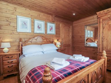 A bedroom with wooden walls a double bed with white linens and folded towels bedside tables with lamps framed pictures and a large mirror at Walnut in Swanage