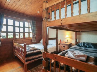 A bedroom with wooden bunk beds and a single bed near a window with checkered curtains at Walnut in Swanage