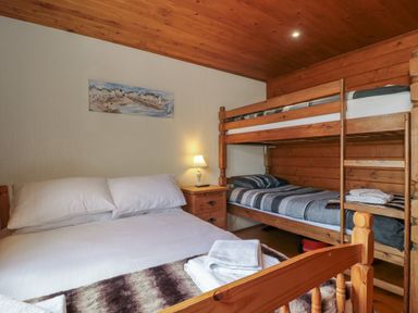 A bedroom with a double bed and wooden bunk beds a bedside table with a lamp and towels on the bed at Walnut in Swanage