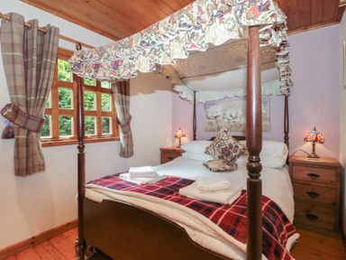 A bedroom with a four poster bed with floral canopy and pillows two bedside tables with lamps and checked curtains at Walnut in Swanage
