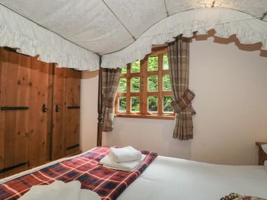 A bedroom with a four-poster bed with a canopy next to a window with check curtains and a wooden wardrobe in Walnut Swanage