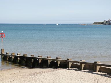 A sandy beach with a wooden groyne extending into the sea and boats on the water at Walnut in Swanage