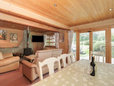A wooden living room with beige sofas a fireplace a dining table with chairs and glass doors leading outside at Pine in Swanage