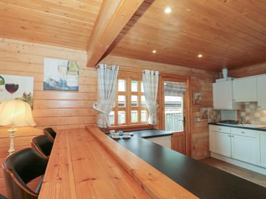 A wooden kitchen with bar stools a countertop a window with curtains and a door at Pine in Swanage