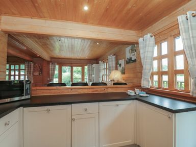 A kitchen with white cabinets a microwave a lamp and windows with curtains at Pine in Swanage