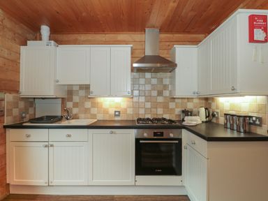 A kitchen with white cabinets black countertops a built in oven gas stovetop a sink and a fire blanket on the wall at Pine in Swanage