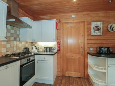 A kitchen with wooden walls and ceiling white cabinets gas stove oven and toaster at Pine in Swanage