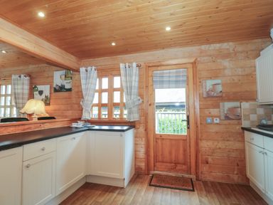 A kitchen with white cabinets black countertops a wooden door with a window and checked curtains at Pine in Swanage