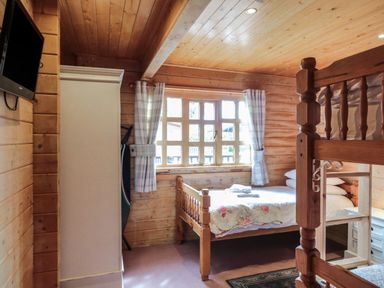 A wooden bedroom with a single bed under a window and bunk beds a wardrobe and a wall-mounted tv at Pine in Swanage