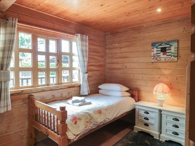 A bedroom with a single bed white bedding bedside cabinet with lamp and window with curtains at Pine in Swanage