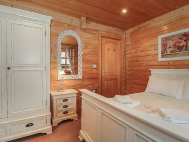 A bedroom with wooden walls a white bed a white wardrobe a bedside table with a lamp and a mirror on the wall at Pine in Swanage