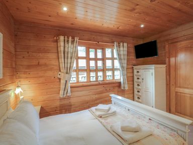 A bedroom with a wooden interior a bed with white linens a window with plaid curtains a white cabinet and a wall-mounted TV at Pine in Swanage