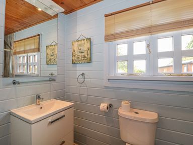 A bathroom with a sink cabinet a mirror a window with blinds and a toilet at Pine in Swanage