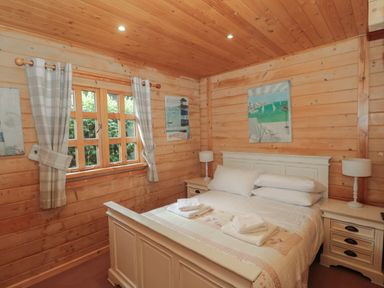 A bedroom with a white bed and two bedside tables with lamps in a wooden cabin at Pine in Swanage