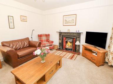 A living room with a brown leather sofa a red plaid armchair a wooden coffee table with flowers a fireplace and a television on a wooden stand at Crookham Dairy Crookham near Etal