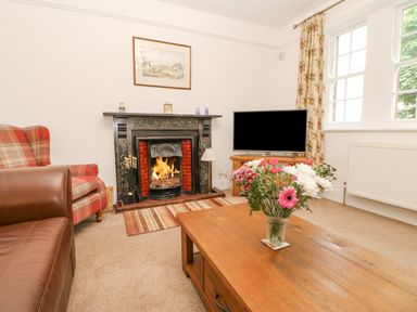 A living room with a fireplace a television a wooden coffee table with flowers and armchairs at Crookham Dairy Crookham near Etal