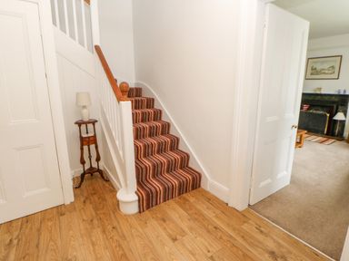 A staircase with striped carpet next to a small wooden table with a lamp and an open door leading to a living room with a fireplace at Crookham Dairy in Crookham near Etal