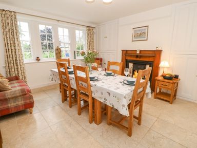 A dining room with a wooden table set for six people with a fireplace and a plaid sofa at Crookham Dairy Crookham near Etal