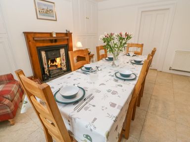 A dining room with a set table and a fireplace with a fire burning at Crookham Dairy Crookham near Etal
