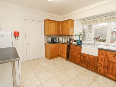 A kitchen with wooden cabinets a white sink a microwave and a window with view outside at Crookham Dairy Crookham near Etal