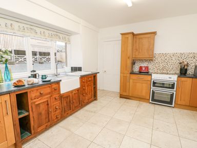 A kitchen with wooden cabinets a white double oven a sink under a window with bread and a coffee set on the counter at Crookham Dairy in Crookham near Etal