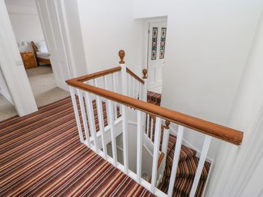 A hallway with striped carpet and wooden banisters with white spindles overlooking a staircase at Crookham Dairy Crookham near Etal