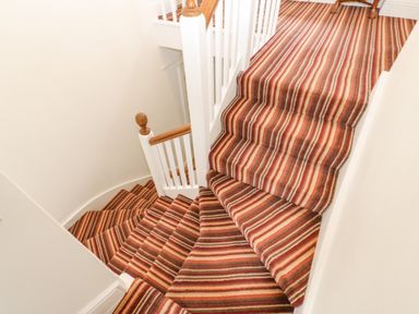 A staircase with striped carpet and white wooden banisters at Crookham Dairy in Crookham near Etal