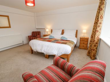 A bedroom with a double bed two bedside tables with lamps two striped armchairs a window with floral curtains and a wall mirror at Crookham Dairy in Crookham near Etal